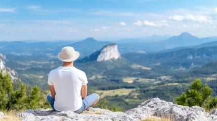 Man sits meditating on mountaintop, vast view