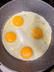 Close-up of four raw eggs sizzling in a nonstick pan, showcasing vibrant yolks and cooking texture in a home kitchen setting.