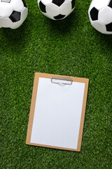 A soccer balls and clipboard on a lush green grassy surface. Top view. Copy space.