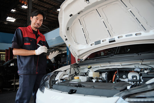 EV car check, portrait of Asian male mechanic worker inspecting and maintaining electric engine battery in fixed automobile garage station, professional technology transportation industry business.