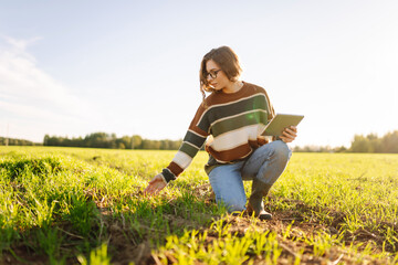 Young female farmer with a digital tablet inspects young plants in an agricultural field. Female...
