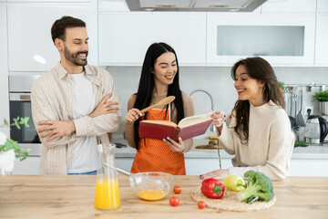 Fototapeta premium Friends gather to explore a cookbook while enjoying an engaging cooking session in a modern kitchen, highlighting teamwork.