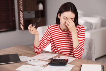 Woman with laptop and calculator paying bills at wooden table indoors