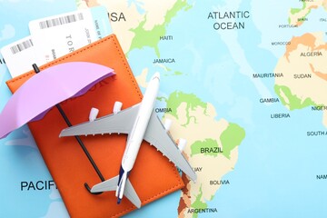 Travel insurance. Plane model, passport, tickets and small umbrella on world map, flat lay. Space...