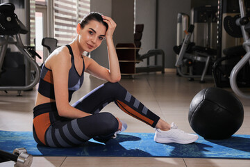 Young woman with medicine ball sitting on mat in gym