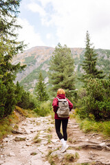 Naklejka premium Woman traveler with backpack walking along rocky hiking trail in mountains. Happy woman enjoying nature and feeling freedom in open air. Hiking, adventure concept.
