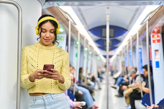 Young woman using smartphone and listening music on subway train