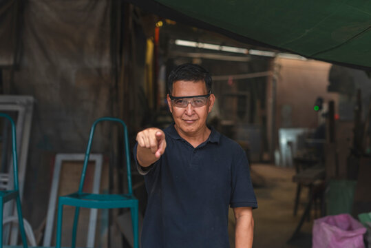 Confident craftsman in a modest workshop points directly at the camera, conveying motivation, encouragement, and focus in skilled trades.