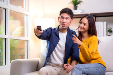 Happy young asian couple sitting on cozy sofa watching TV together and enjoying a relaxation in...