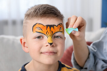 Animator drawing tiger on boy's face indoors, closeup