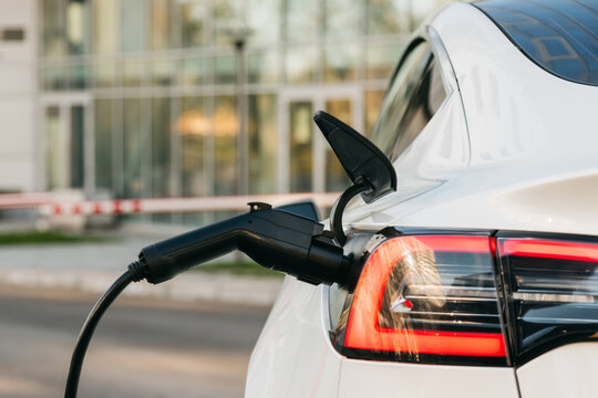 Close-up of a white electric car charging in a street parking. Environmentally friendly transport in the urban environment. Clean energy.