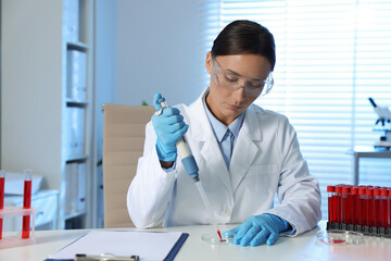 Laboratory testing. Doctor dripping blood sample into Petri dish at table indoors