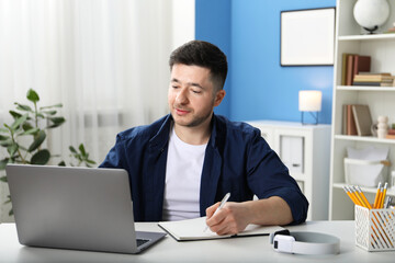 Fototapeta premium Man taking notes during online lesson at desk indoors. Self-study