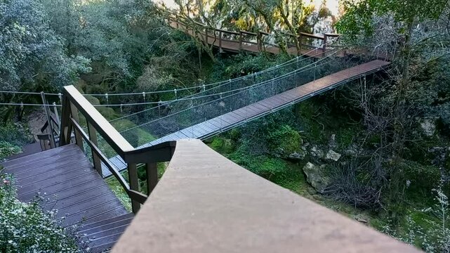 Wooden walkways and a suspension bridge on the mountain slopes of the Mouros River Waterfall in Condeixa-a-Nova, Portugal, a fantastic trail surrounded by nature in shades of green and brown.