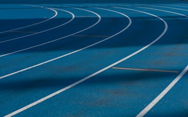 A blue running track with white lines, curving towards the horizon, symbolizing the pursuit of goals and progress.