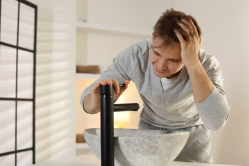 Unhappy young man suffering from hangover near sink in bathroom