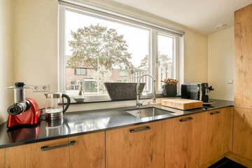 A stylish kitchen featuring natural light streaming through large windows, highlighting contemporary appliances and wooden cabinetry.