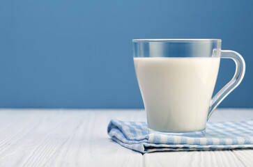 milk in glass cup resting on checkered cloth on white wooden table with blue background