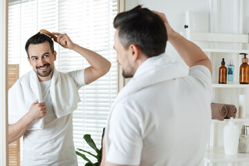 Obraz premium Handsome man styling his hair with comb near mirror at home