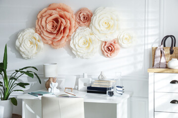 Beautiful decorative paper flowers on white wall and stylish furniture indoors