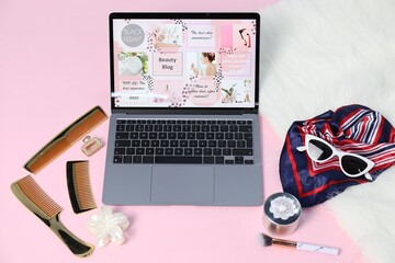 Laptop with beauty blog web site and different accessories on pink background, above view