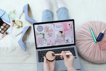 Blogger holding face powder and brush near laptop with beauty blog web site on floor indoors, above...