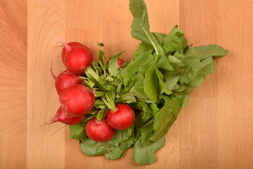 A bunch of fresh, vibrant red radishes with green leaves rests on a light wooden surface, captured in a close-up, top-down shot