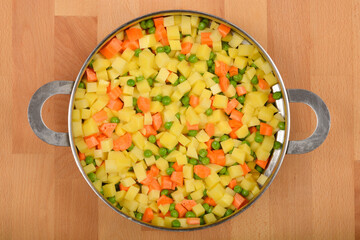 Raw diced potatoes, carrots, and peas are mixed together in a steamer basket, viewed in a close-up, top-down shot