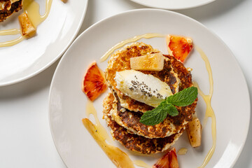 Cottage cheese pancakes with cream cheese, orange, honey and mint on a white plate and background. Healthy, dietary breakfast. Top view