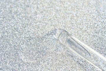 Transparent glass dropper on sparkling silver glitter background texture shine.