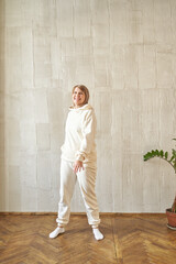 Smiling caucasian female adult in comfortable cream tracksuit standing on wooden floor.