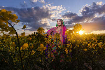 Young girl in national Afghan costume dancing in a field with yellow rapeseed flowers