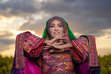 Young woman in national Afghan costume dancing in a field with yellow rapeseed flowers