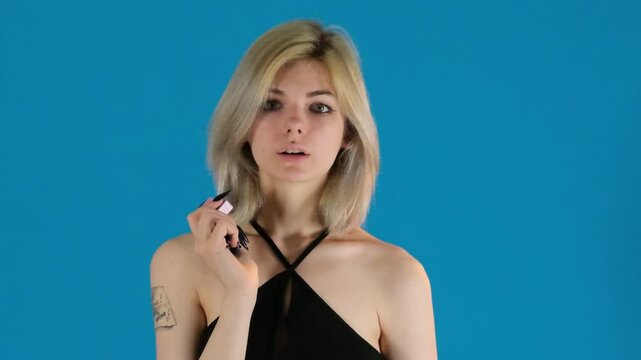 Young woman smoker inhales vaper on blue background. Blonde female playfully exhales dense smoke enjoying process of smoking slow motion