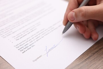 Man putting signature on document at wooden table, closeup