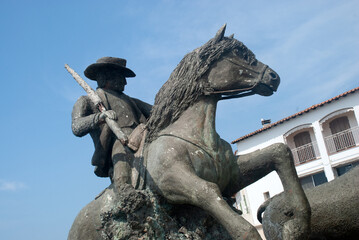 Statue of man in hat riding horse near bull in sunlight, Les Saintes Maries de la Mer Camargue, France