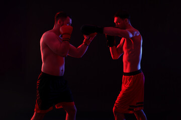 Men in boxing gloves fighting on black background in neon lights