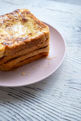 Close-up of buttered french toast with syrup and honey on pink plate