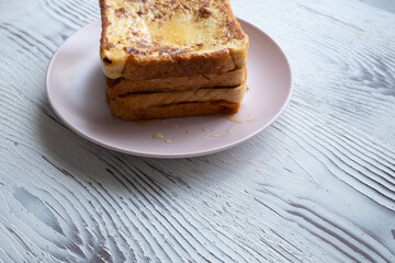 Close-up of buttered french toast with syrup and honey on pink plate