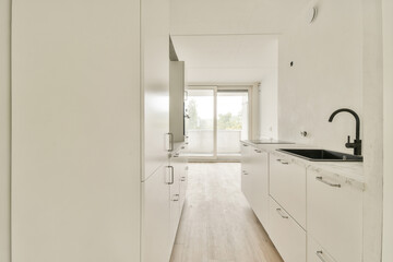 A sleek, modern kitchen featuring white cabinets, minimalistic design, and natural light flowing through large windows, creating an inviting atmosphere.