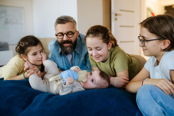 Three sisters looking at newborn brother in fathers arms.