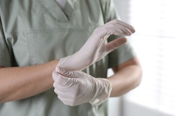 Medical worker putting on gloves in hospital, closeup