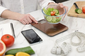 Woman with smartphone weighting salad at white table indoors, closeup