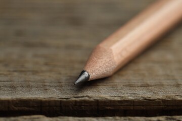One sharp graphite pencil on wooden table, closeup. Space for text