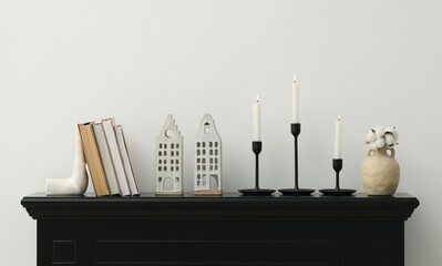 Stylish candlesticks with burning candles and other decor on fireplace near white wall indoors