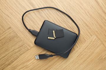 External hard drive with USB cable and SD memory cards on light wooden table, top view