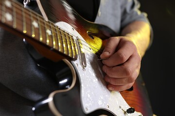 Man playing guitar with mediator on black background, closeup