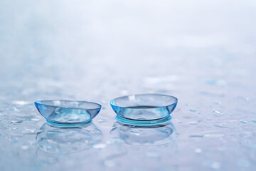 Pair of contact lenses and water drops on light mirror surface, closeup