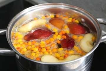 Making compot of apples and sea buckthorn berries. Simmering fruits in pot on stove, closeup