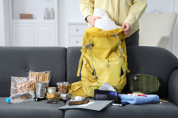 Survival kit. Woman putting clothes into backpack indoors, closeup